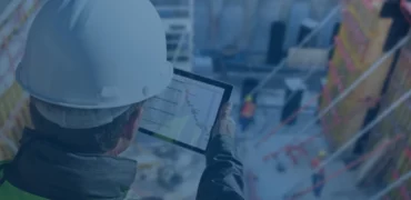 Person in hard hat looking at a tablet with construction site i the background